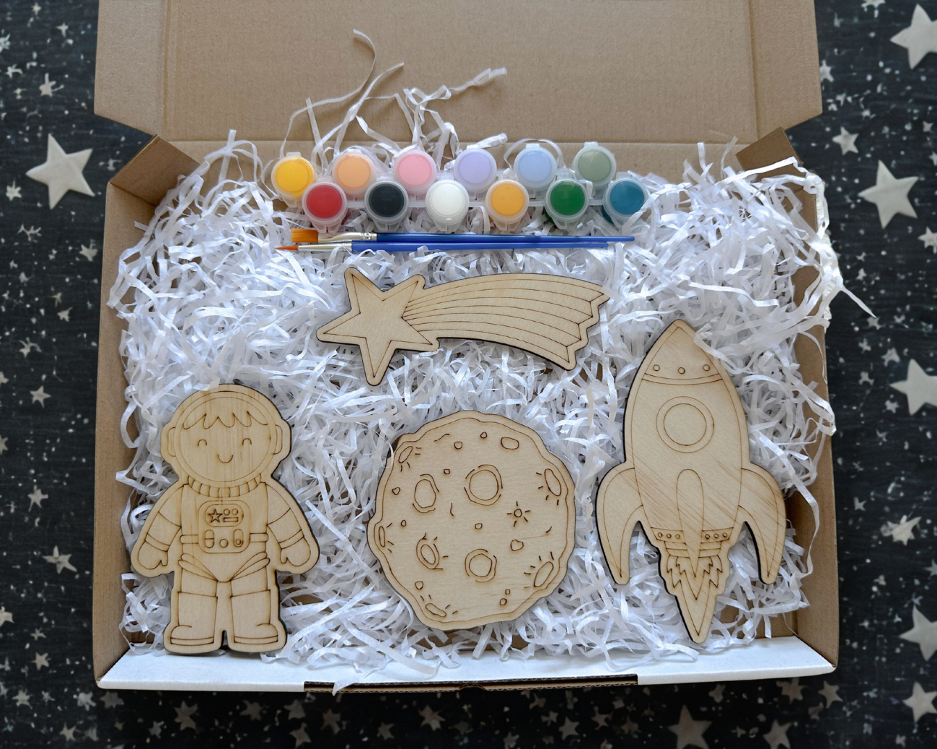 Wooden space-themed craft kit with paint and brushes on a starry background