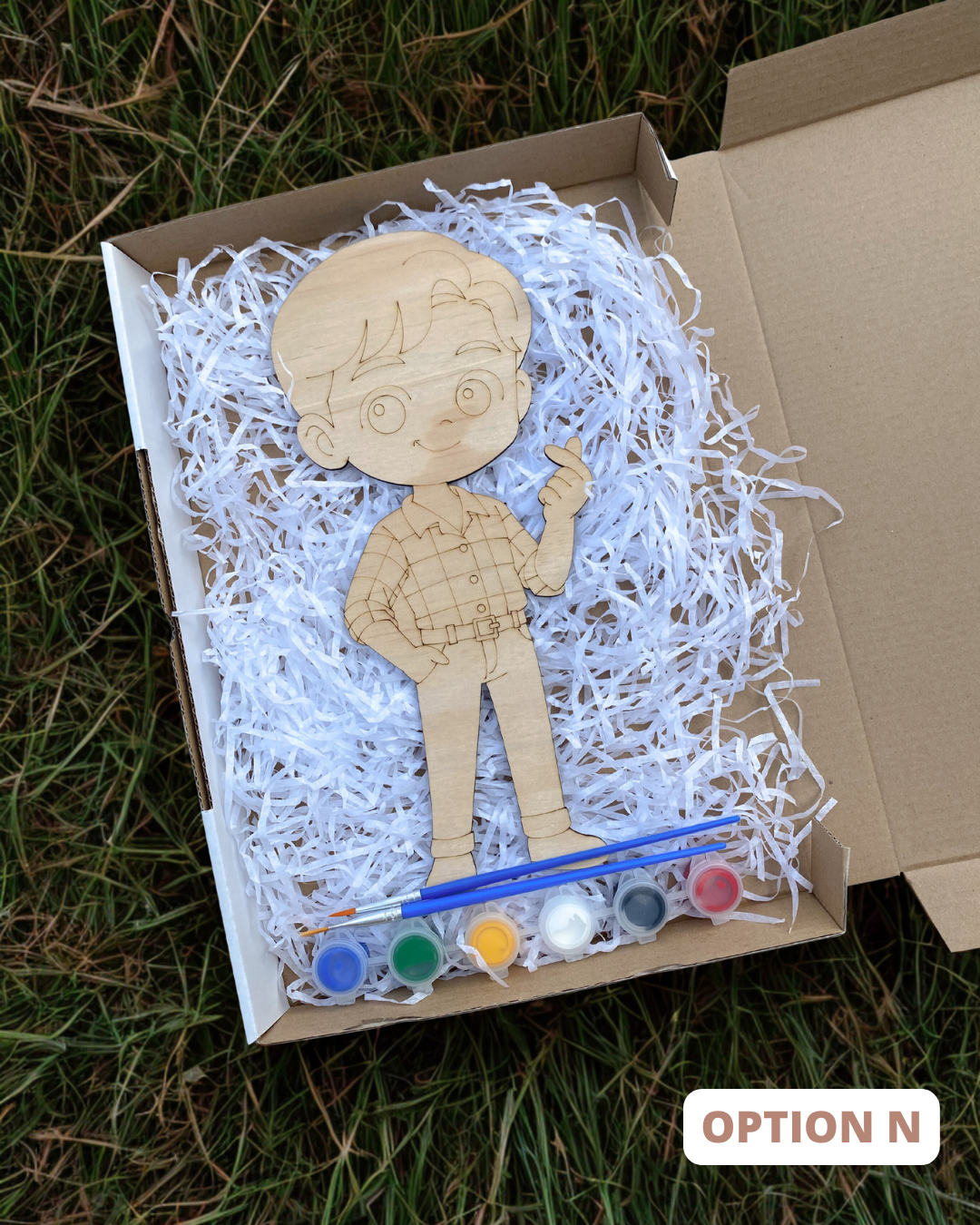 Wooden boy figure with paint supplies in a box on grass