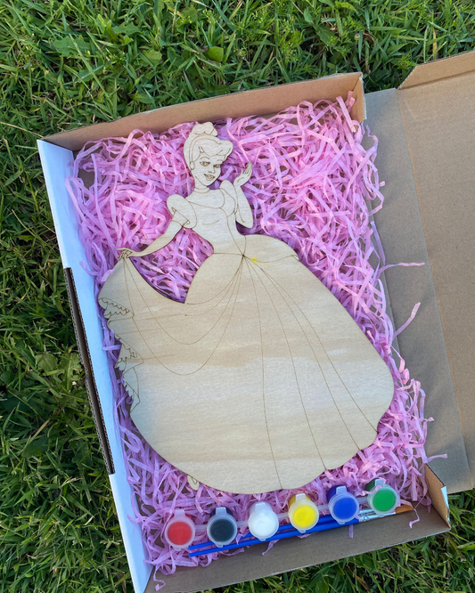 Wooden Cinderella figure in a box with pink filler and paint supplies on grass
