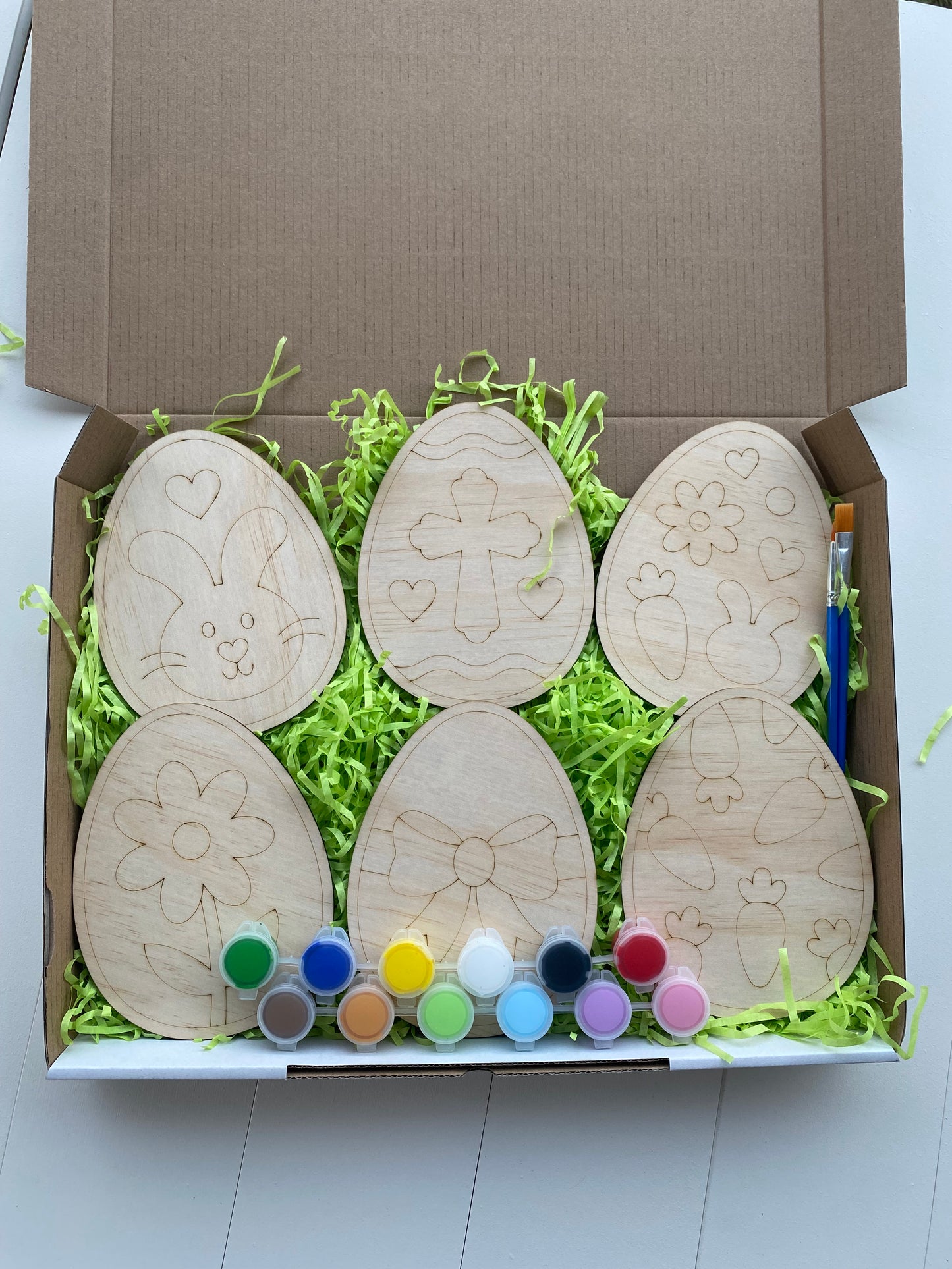 Wooden Easter egg-shaped canvases with paint supplies in a box