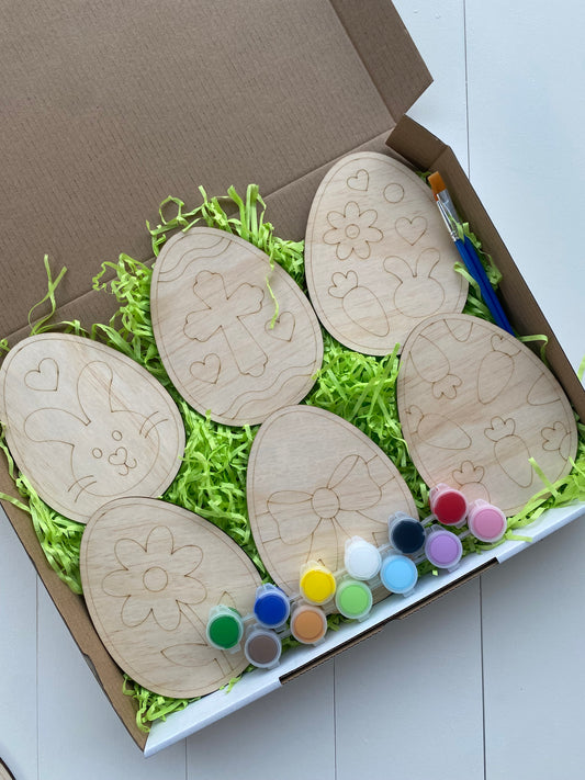 Wooden Easter egg-shaped crafts with paint supplies in a box