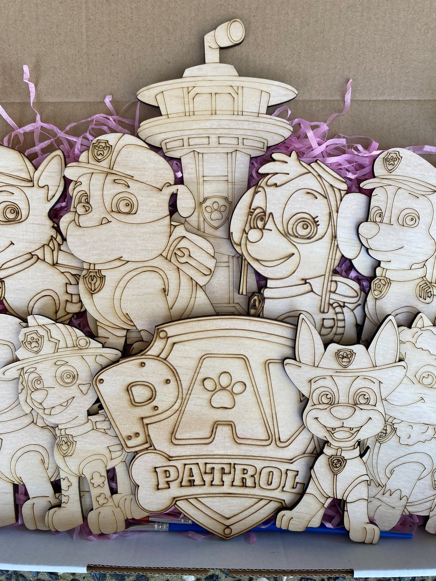 Wooden toys resembling characters from a popular children's show, displayed in a box with purple tissue paper.