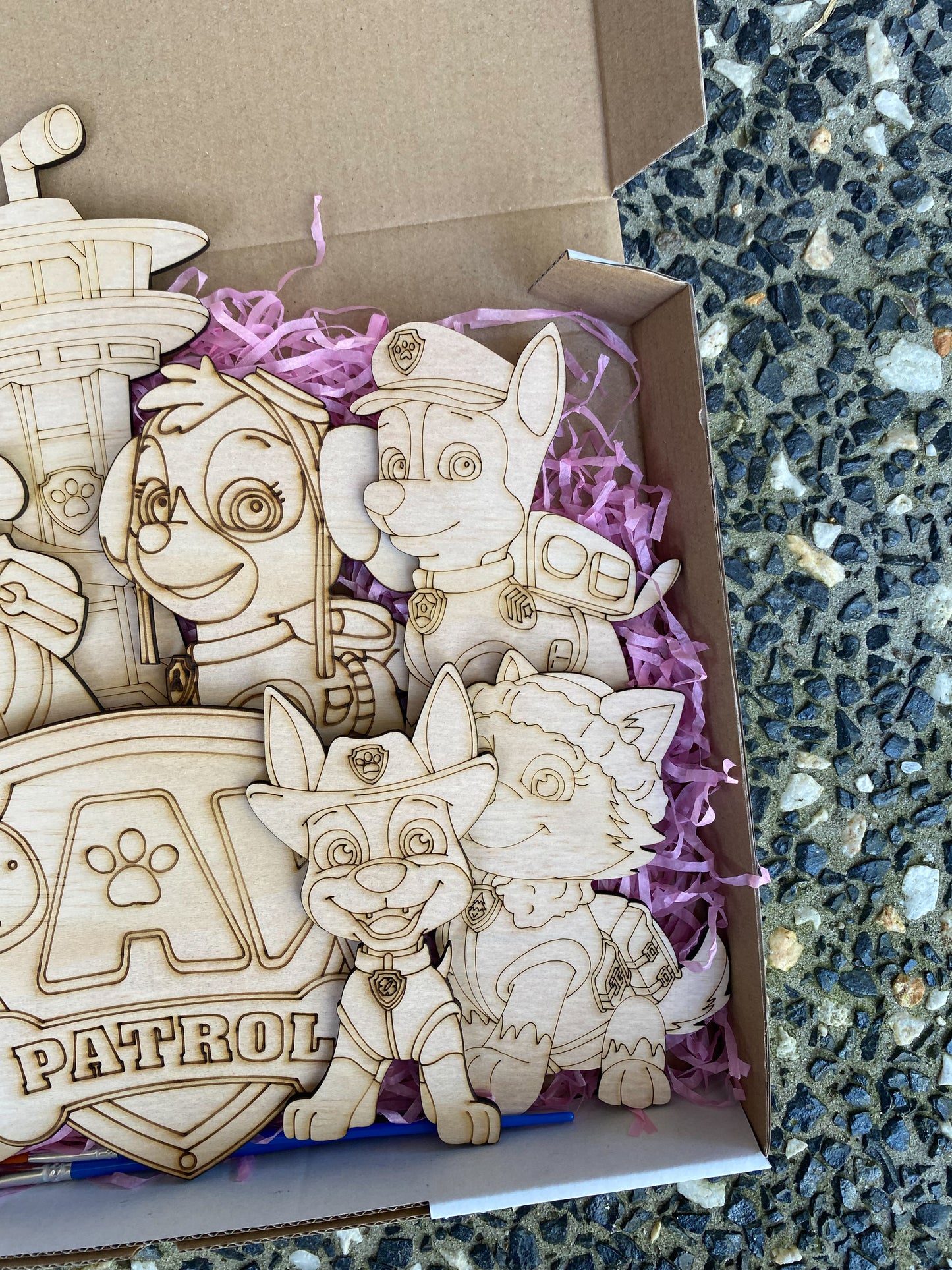 Wooden toys resembling characters from a popular children's show, displayed in a box with purple tissue paper.