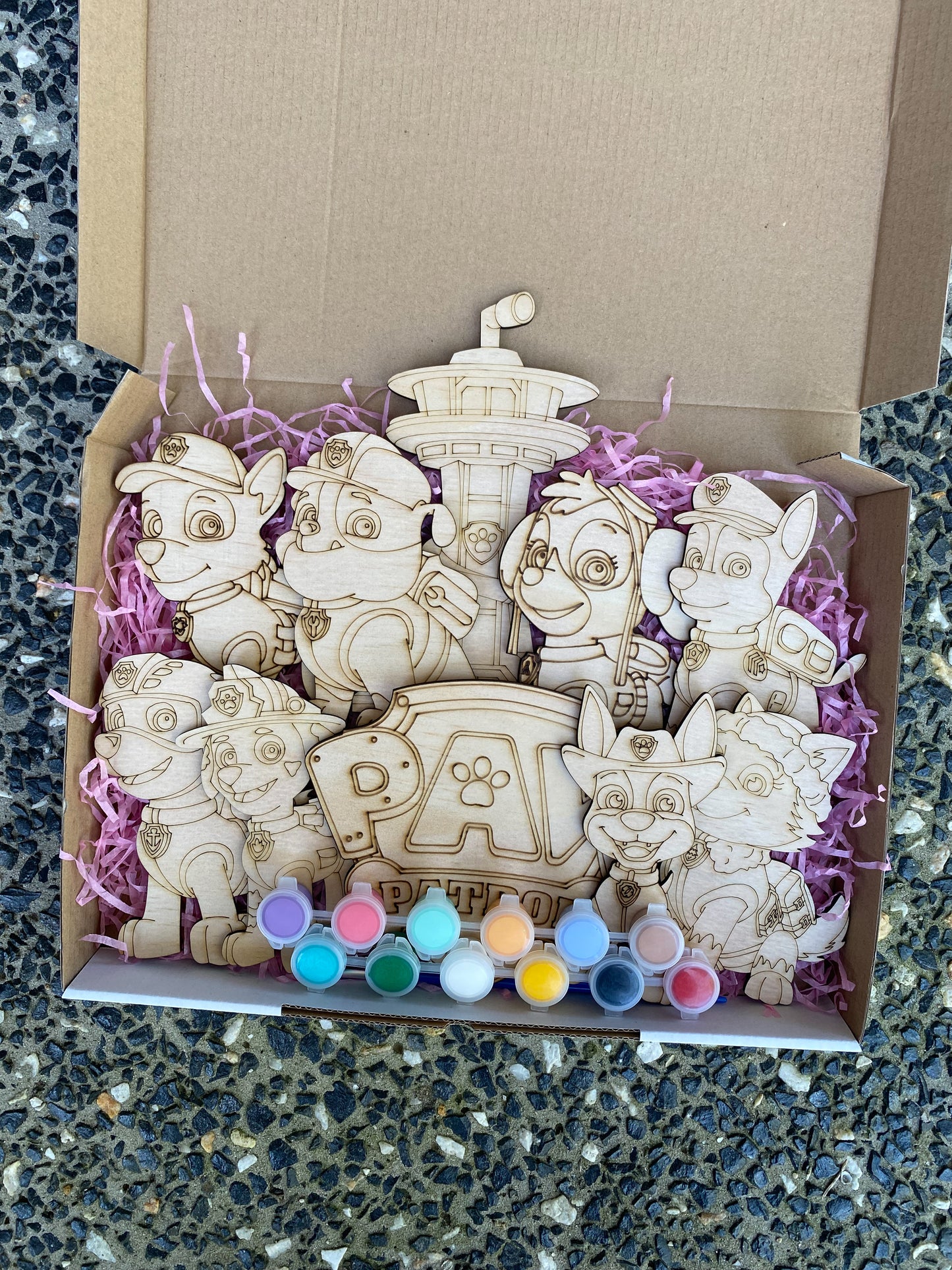 Wooden toys resembling characters from a popular children's show, displayed in a box with purple tissue paper.