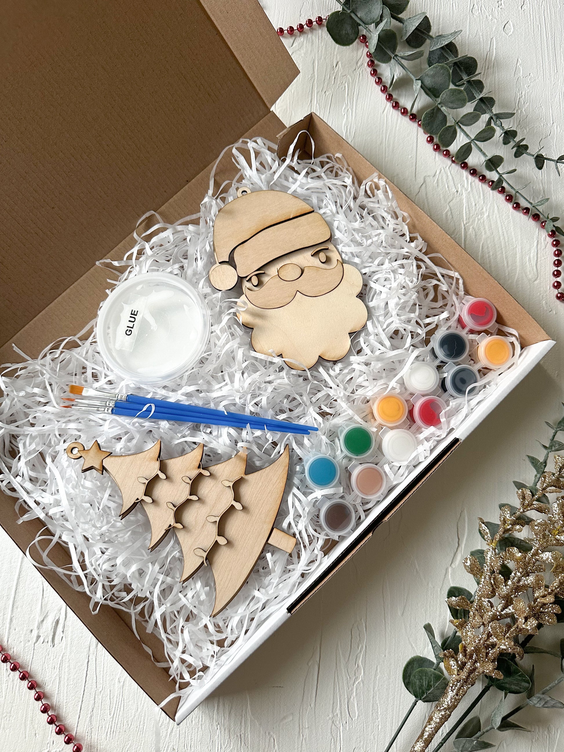 Craft kit with wooden Santa Claus ornament, paint, and brushes in a box.