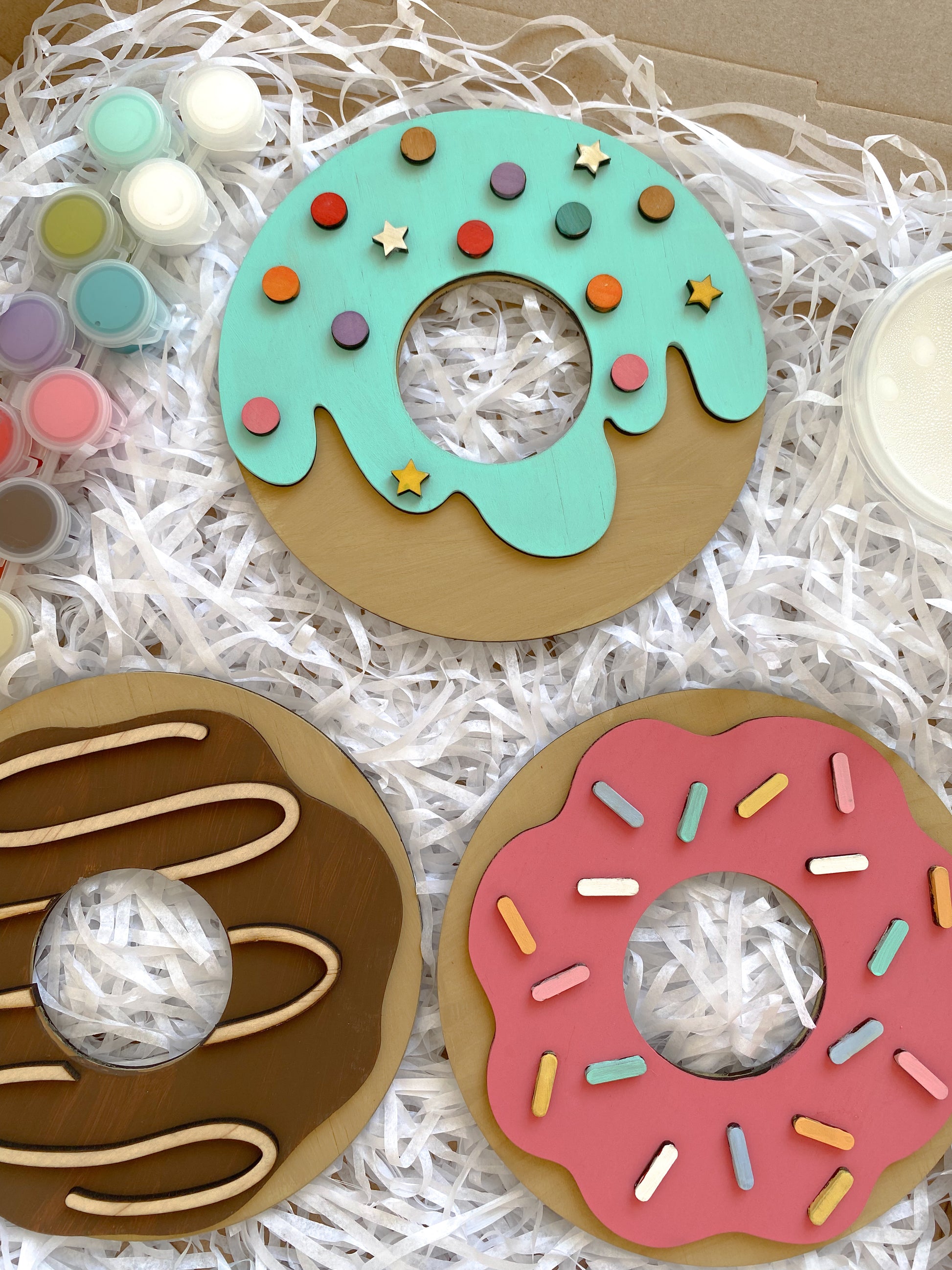 Three decorative donut-shaped items with colorful sprinkles on a white shredded paper background.