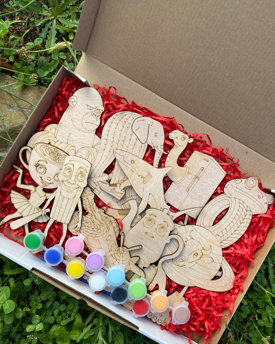 Wooden Brain Rot figures in a box with paint pots on a red shredded paper background