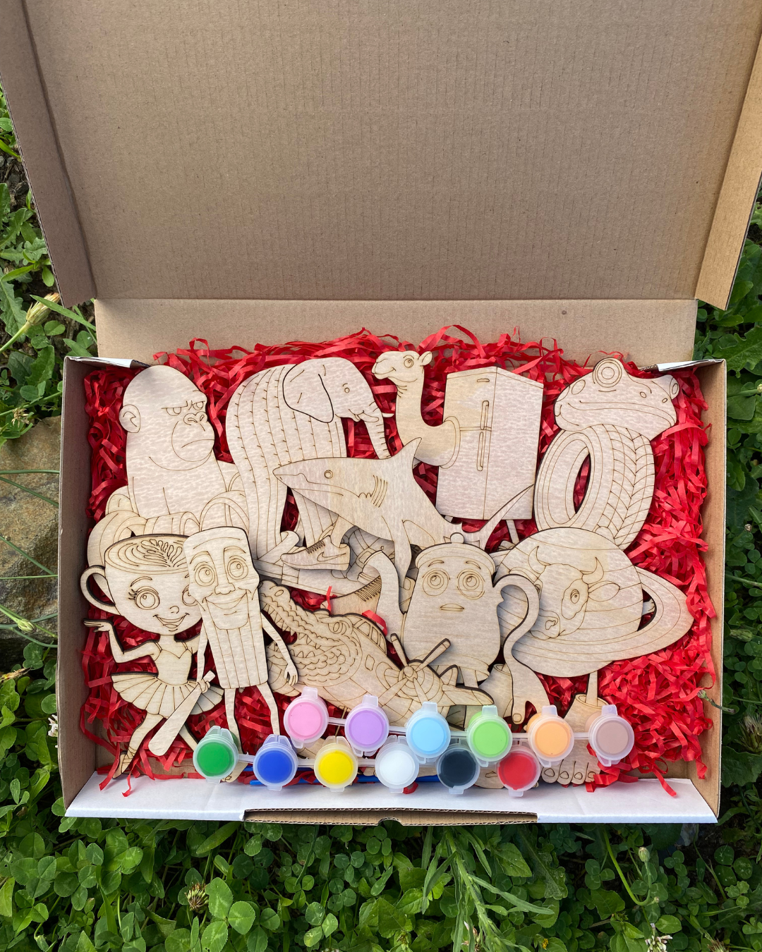 Wooden Brain Rot figures in a box with paint pots on a red shredded paper background