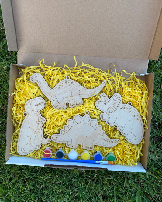 Box of wooden dinosaur toys with paint supplies on a grassy background